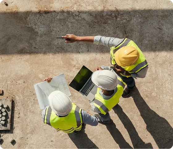 Aerial view of two construction workers in hard hats pointing at site plans