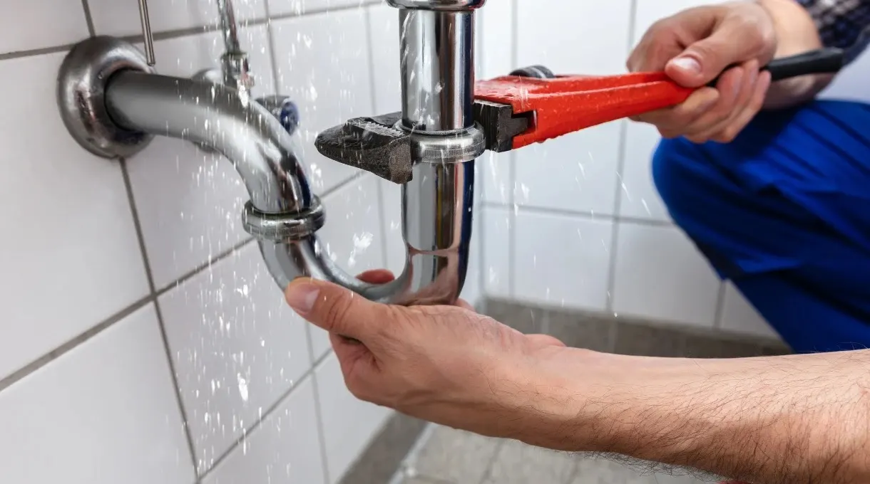 Technician using a wrench to repair a leaking pipe under a sink