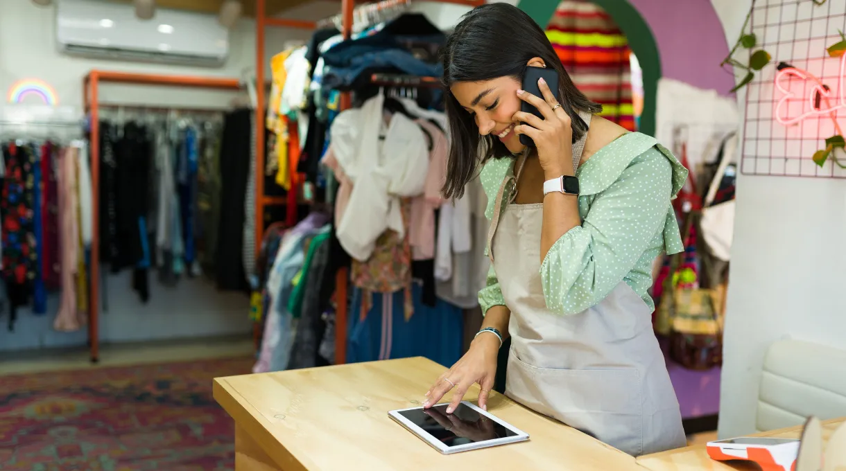 Retail store employee on the phone while using a tablet at the checkout counter