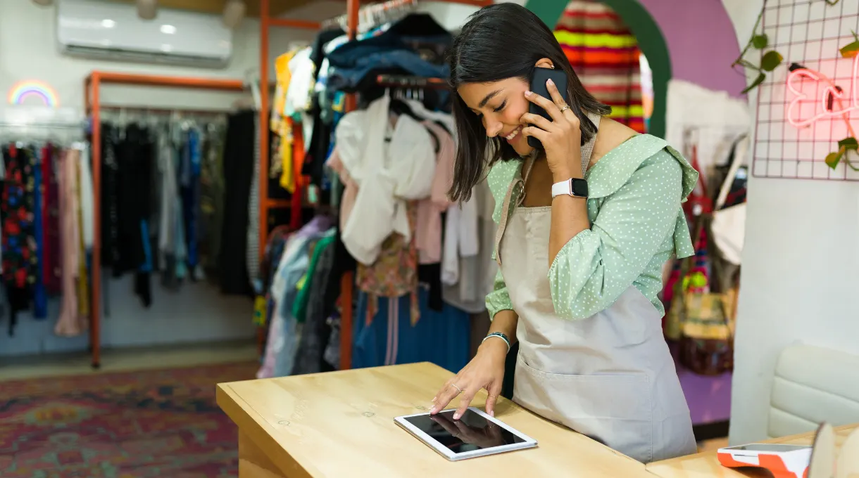 Retail store employee on the phone while using a tablet at the checkout counter