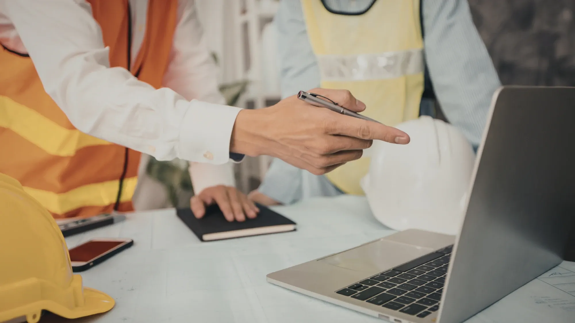 Two team members in safety vests reviewing plans on a laptop